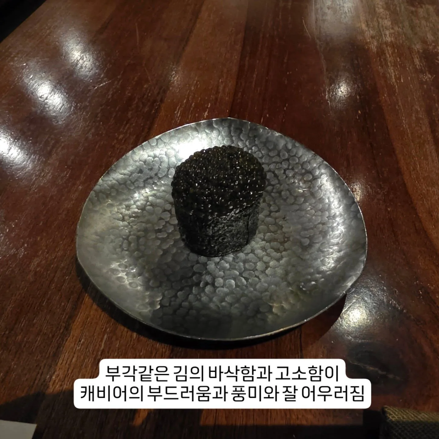 A small caviar-topped course on a dark plate at JUA
